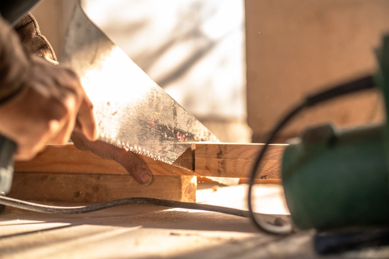services-03 Carpenter cutting wood with a hand saw, showcasing craftsmanship and precision.